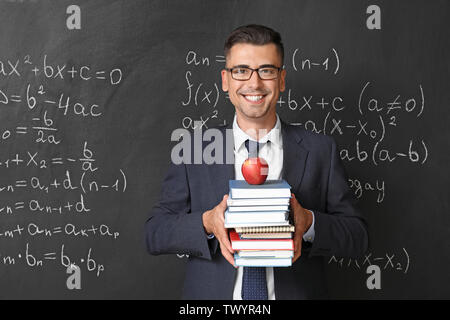 Handsome math teacher with books near blackboard in classroom Stock Photo