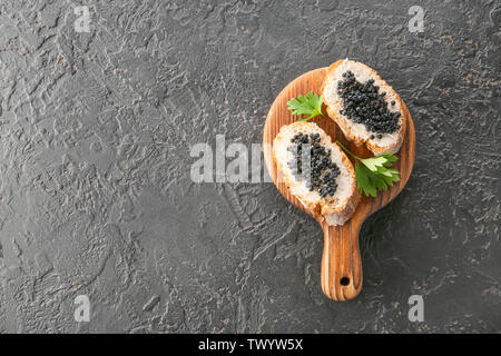 Wooden board with delicious black caviar on dark background Stock Photo