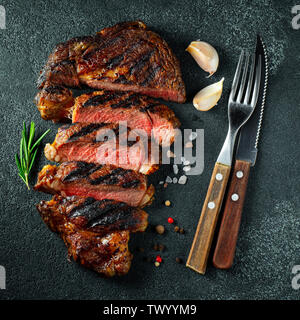 Sliced steak ribeye, grilled with pepper, garlic, salt and thyme on a dark stone background. Top view. Flat lay Stock Photo