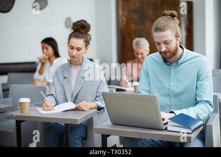 Portrait of contemporary bearded man using laptop in class with group of students enjoying lecture, copy space Stock Photo