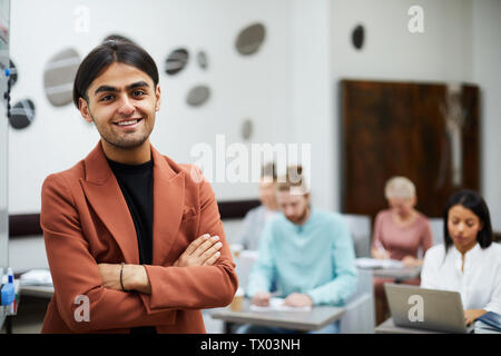 Waist up portrait of mixed-race young man smiling at camera confidently with group of students in background, copy space Stock Photo