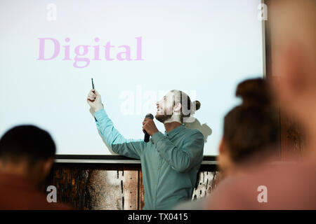 Waist up portrait of contemporary bearded man giving presentation pointing at word DIGITAL on projector screen during lecture, copy space Stock Photo