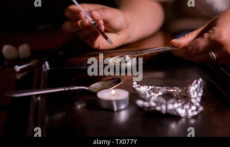 Person preparing heroin with a needle, spoon, candle and foil.