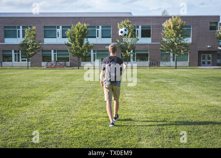 Teenager tossing a soccer ball in the air as he walks through an empty soccer field. Stock Photo