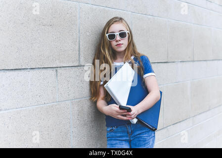 Lonely teenage girl leaning against brick wall while texting on her phone. Stock Photo