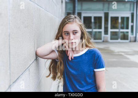 Sad teenage girl leaning against a brick wall. Stock Photo