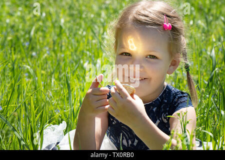 Little girl holding a bitcoin cryptocurrency coin in hands. A child plays with gold coins sitting on the grass Stock Photo