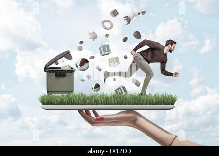 Woman's hand holding ipad with green grass growing on screen and man running from things flying out of trash can that is standing on grass. Alarming g Stock Photo