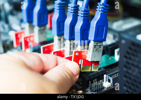 Close-up hand plug a cable to slot for build a equipment for mining cryptocurrency as altcoins or bitcoin. Connectors on motherboard for graphic cards Stock Photo