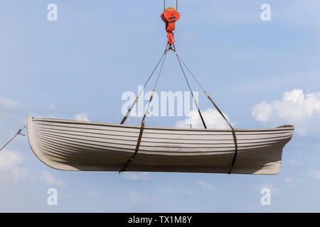 Rowing boat hanging on a crane hook on a blue sky background Stock Photo