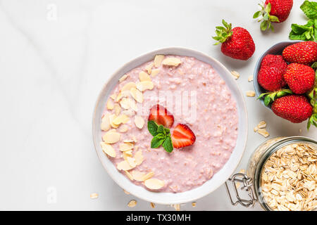 overnight oats with fresh strawberries, almonds and mint in a bowl on white marble table. healthy breakfast. top view Stock Photo