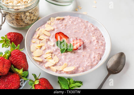 healthy breakfast. overnight oats with fresh strawberries, almonds and mint in a bowl with a spoon on white marble table. close up Stock Photo