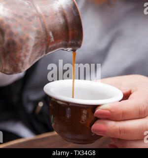 Pouring hot coffee in a ceramic cup with a traditional Turkish copper coffee pot. Stock Photo