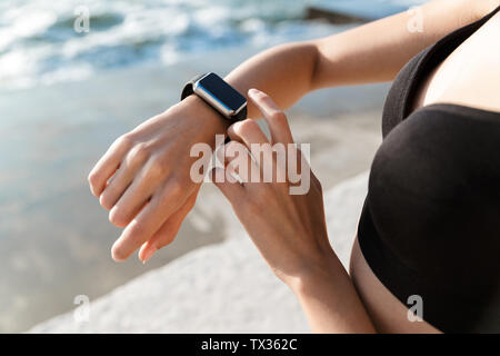 Close up young athlete woman wearing sportswear using smartwatch while standing outdoors Stock Photo