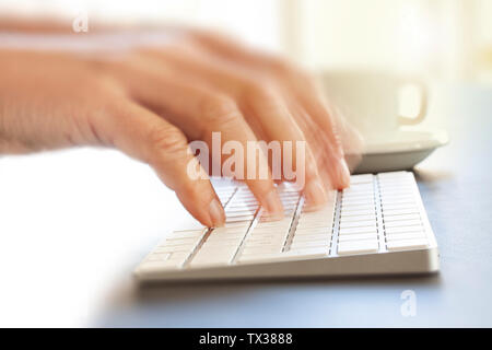 Fingers working on computer keyboard in modern delicate lightning. Hand and fingers blurred as person is working fast. Close up image. Stock Photo