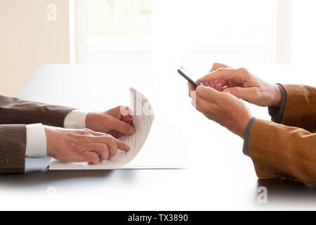 Hands from two businessmen in conversation by a desk. One pointing in some papers and the other texting on a cell phone. Negotiating business or a job Stock Photo