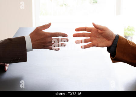Hands from two businessmen in conversation by a desk about to shake hands. Negotiating business or a job interview. - Image Stock Photo