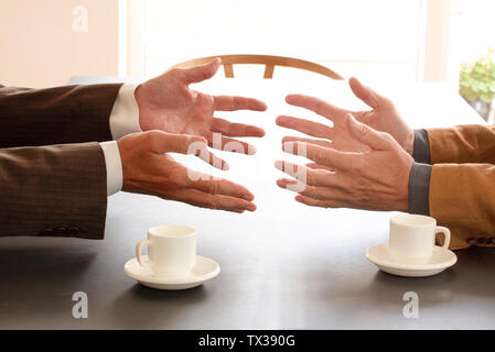 Hands from two businessmen in conversation by a desk. Two cups of coffee on the table. Negotiating business or a job interview. - Image Stock Photo