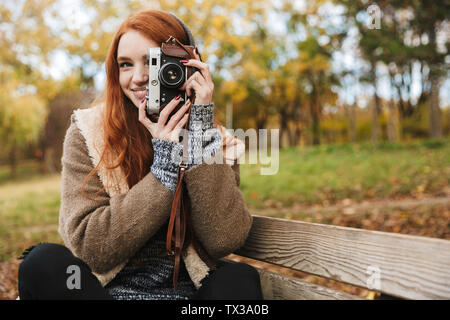 Lovely redheaded young girl listening to music, holding photo camera while standing outdoors Stock Photo
