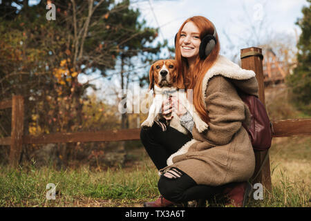 Lovely redheaded young girl listening to music with headpones while playing with her dog at the park Stock Photo
