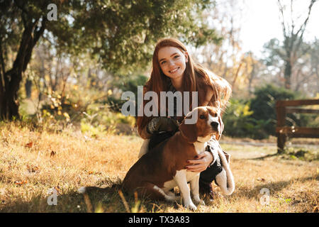 Lovely redheaded young girl listening to music with headpones while playing with her dog at the park Stock Photo