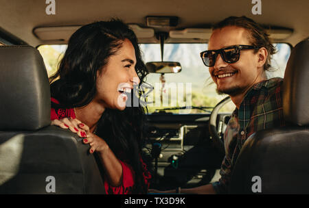 Rear view of a young couple on road trip. Smiling man and woman looking back sitting in a car.