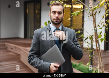 Attractive young businessman wearing suit walking outdoors, carrying laptop computer Stock Photo