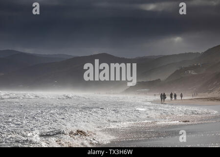 Ominous clouds over silhouetted people walking on ocean beach, Aireys Inlet, Victoria, Australia Stock Photo