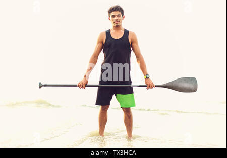 Portrait confident young man holding oar in ocean surf Stock Photo