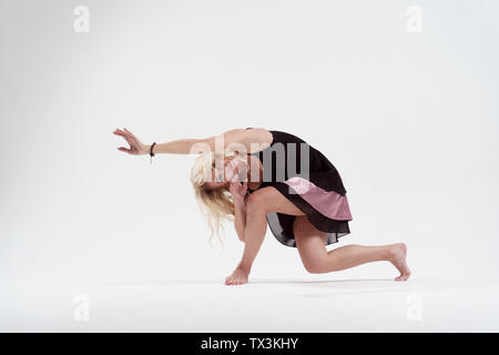 Photo of long-haired blonde looking to side with outstretched hand dancing in studio Stock Photo