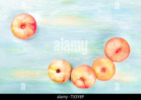 An overhead photo of vibrant organic flat saturn peaches forming a frame, shot from above on a teal background with copyspace Stock Photo
