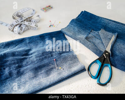 Pant leg with a large hole cut off with scissors from a blue jeans folded in a half. Making denim shorts. On a white background. Stock Photo