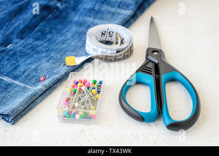 Blue jeans shorts, roll of tailor tape with centimeters and inches, multi coloured headed sewing pins in a box and scissors.  Making denim shorts. On Stock Photo