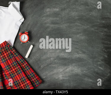 School uniform white shirt skirt plaid alarm clock on the background of chalk board. Concept back to school and education. Top view flat layout. Copy Stock Photo
