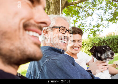 Men of a family sitting on a swing bed ing the garden, talking Stock Photo