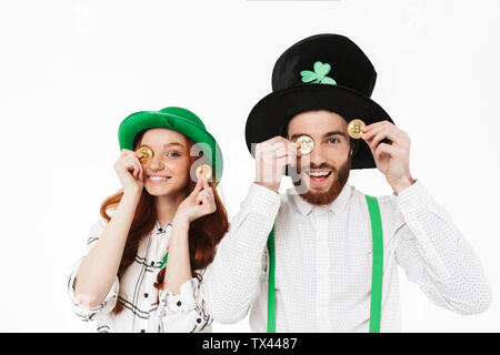 Happy young couple wearing costumes, celebrating St.Patrick 's Day isolated over white background, holding golden bitcoins Stock Photo