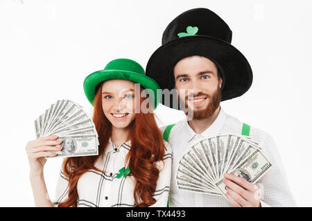 Happy young couple wearing costumes, celebrating St.Patrick 's Day isolated over white background, holding money banknotes Stock Photo