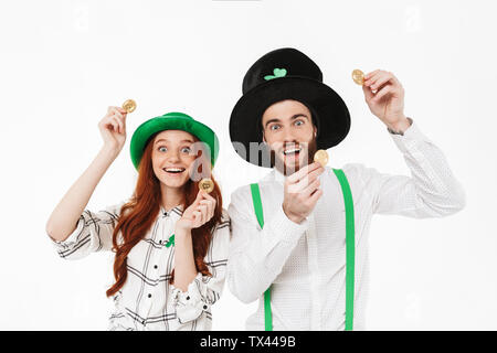 Happy young couple wearing costumes, celebrating St.Patrick 's Day isolated over white background, holding golden bitcoins Stock Photo