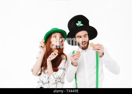 Happy young couple wearing costumes, celebrating St.Patrick 's Day isolated over white background, holding golden bitcoins Stock Photo