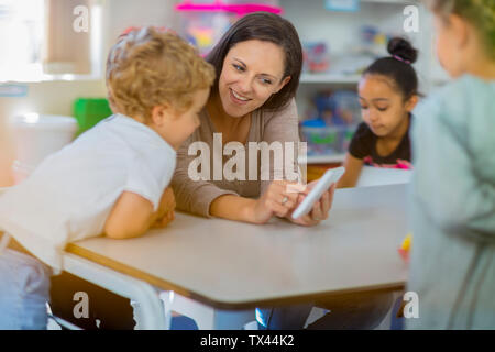 Pre-school teacher showing mini tablet to children in kindergarten Stock Photo