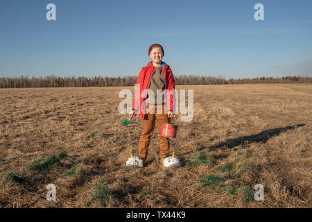 Portrait of smiling boy with paint bucket and brush wearing unicorn slippers in steppe landscape Stock Photo