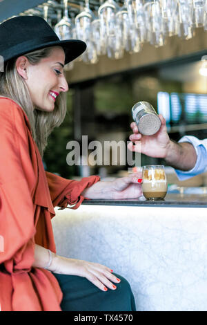 Smiling woman at the counter of a bar watching barkeeper preparing a drink Stock Photo