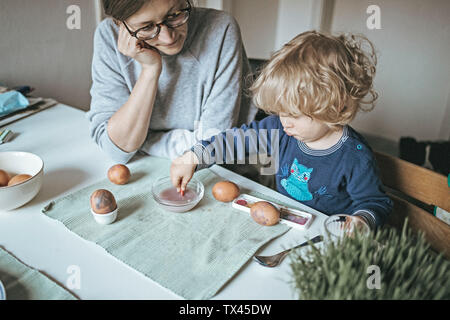 Mother and daughter sitting at table at home painting Easter eggs Stock Photo