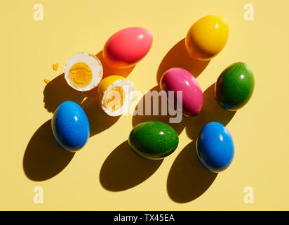 Dyed Easter eggs on yellow background with one broken egg Stock Photo