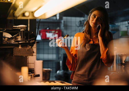Young woman talking on cell phone in restaurant kitchen Stock Photo