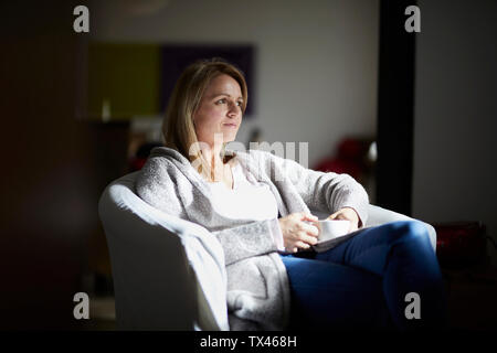 Woman sitting at home, relaxing in arm chair Stock Photo