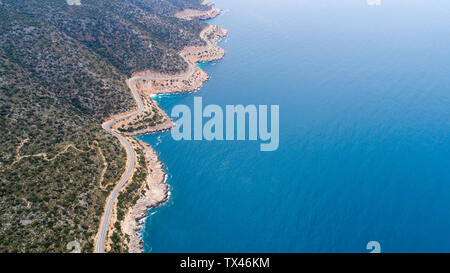 Aerial landscape of coastline and a road seascape. Car drives down the empty asphalt road running along the sunny Mediterranean shoreline of Turkey. Stock Photo