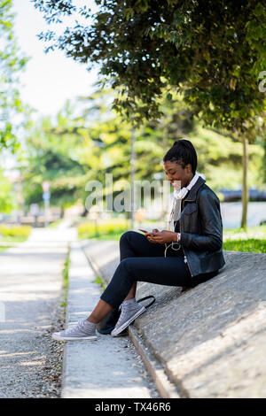 Smiling woman resting in urban park using cell phone Stock Photo