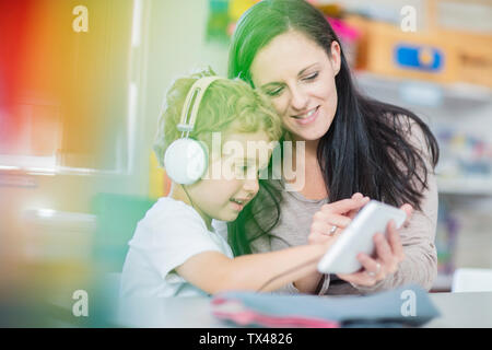 Pre-school teacher showing mini tablet to boy with headphones in kindergarten Stock Photo