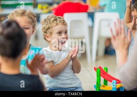 Happy children and pre-school teacher clapping hands in kindergarten Stock Photo